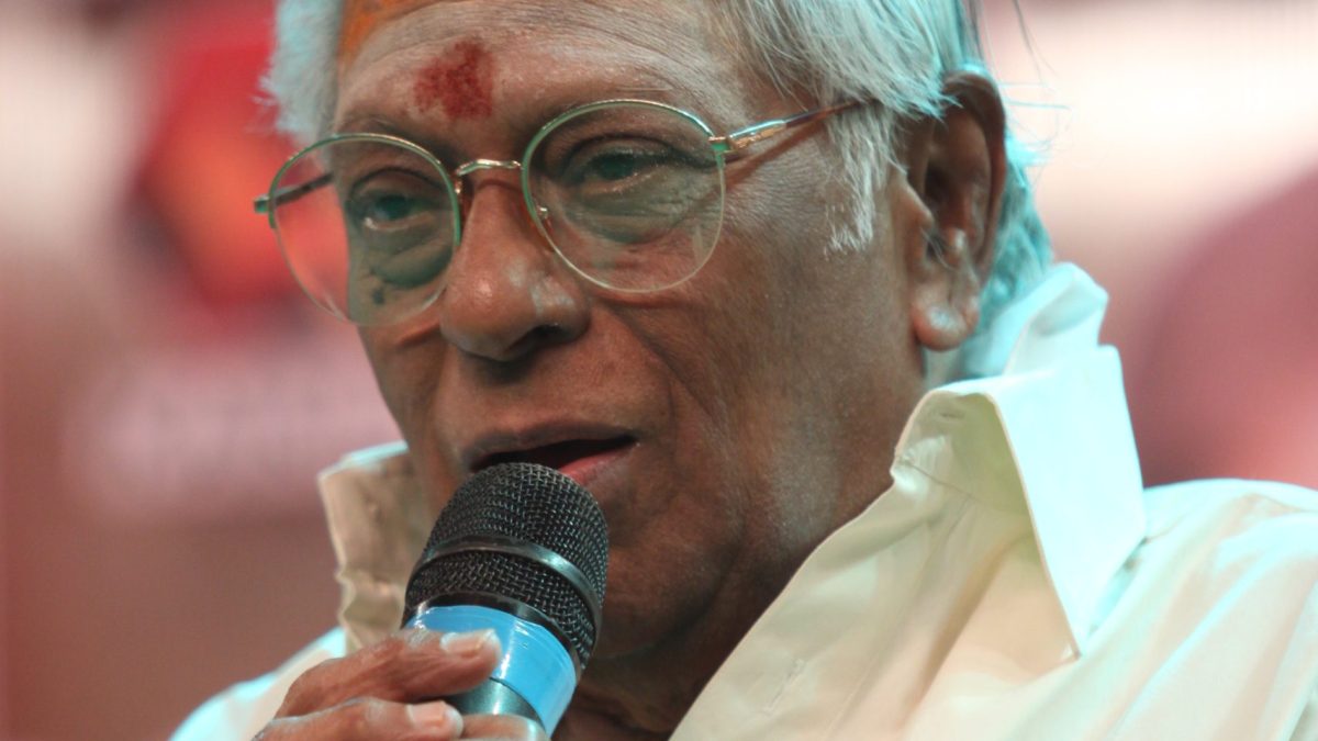 M. S. Viswanathan in a white shirt singing into a microphone