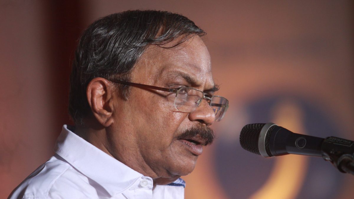 M. T. Vasudevan Nair in glasses and a white shirt speaking at a microphone