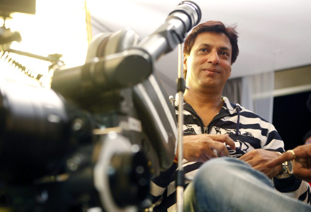 Madhur Bhandarkar in a striped shirt sitting beside a film camera