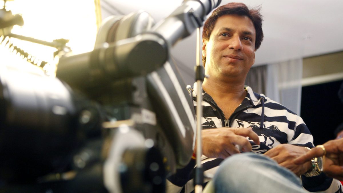 Madhur Bhandarkar in a striped shirt sitting beside a film camera