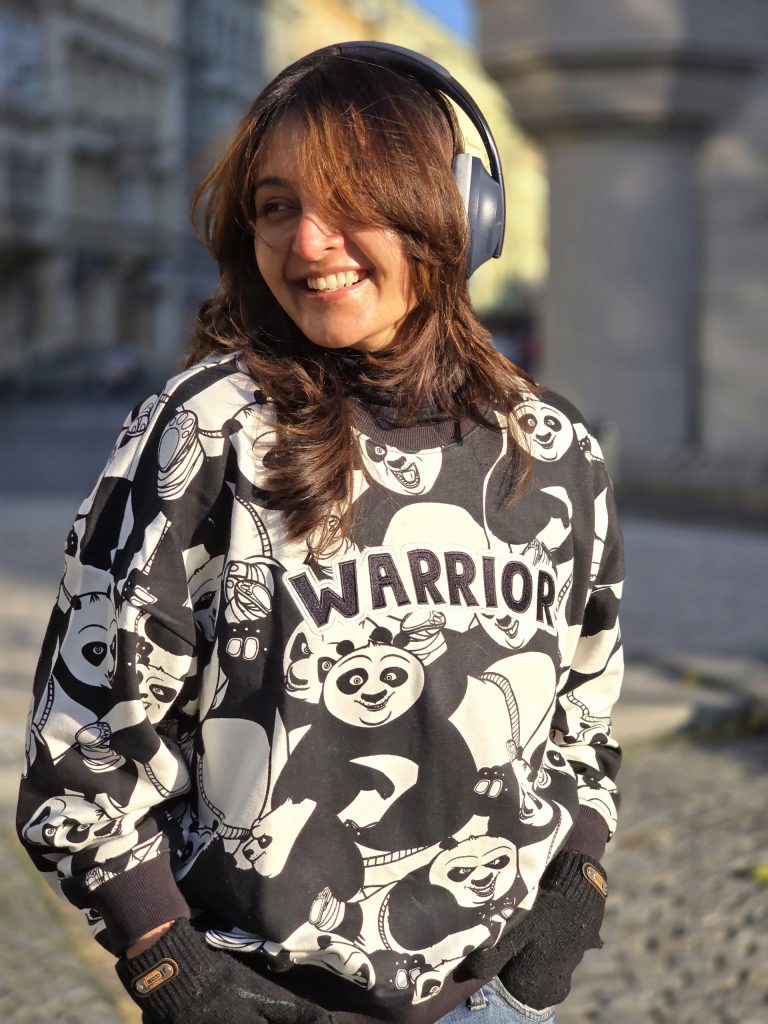 Manju Warrier smiling, wearing headphones around her neck and a printed sweatshirt