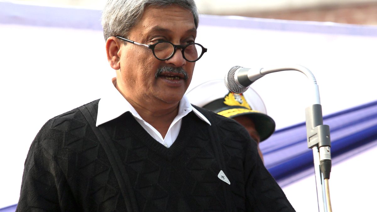 Manohar Parrikar in glasses and a dark jacket speaking at a lectern