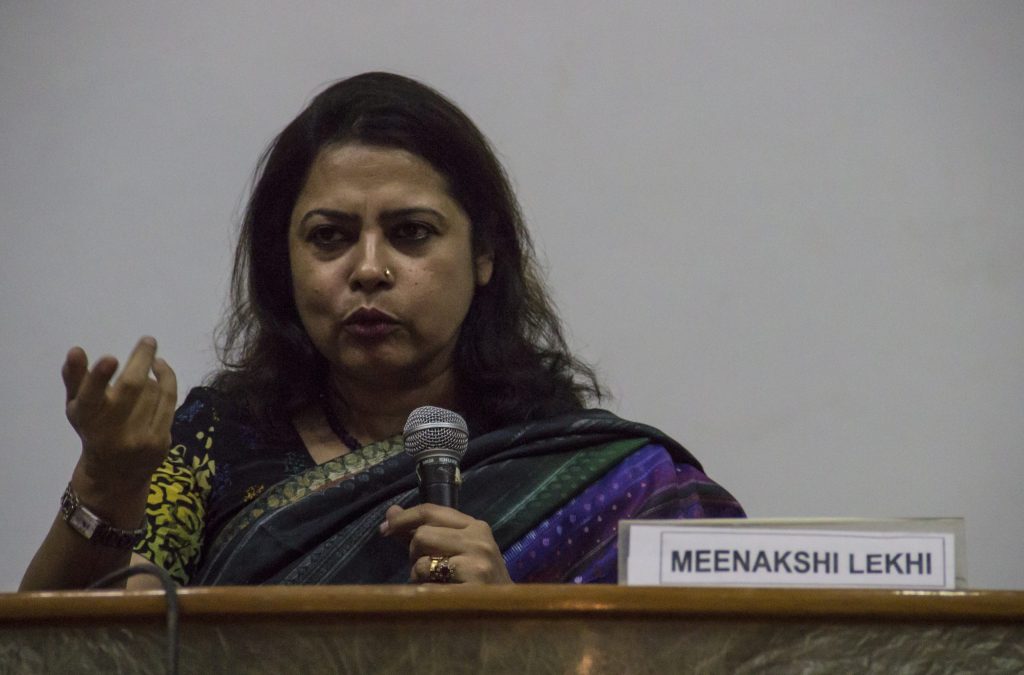 Meenakshi Lekhi in a blue sari speaking into a microphone and gesturing, with her name plate in front