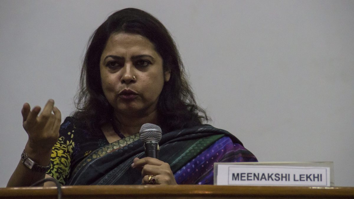 Meenakshi Lekhi in a blue sari speaking into a microphone and gesturing, with her name plate in front
