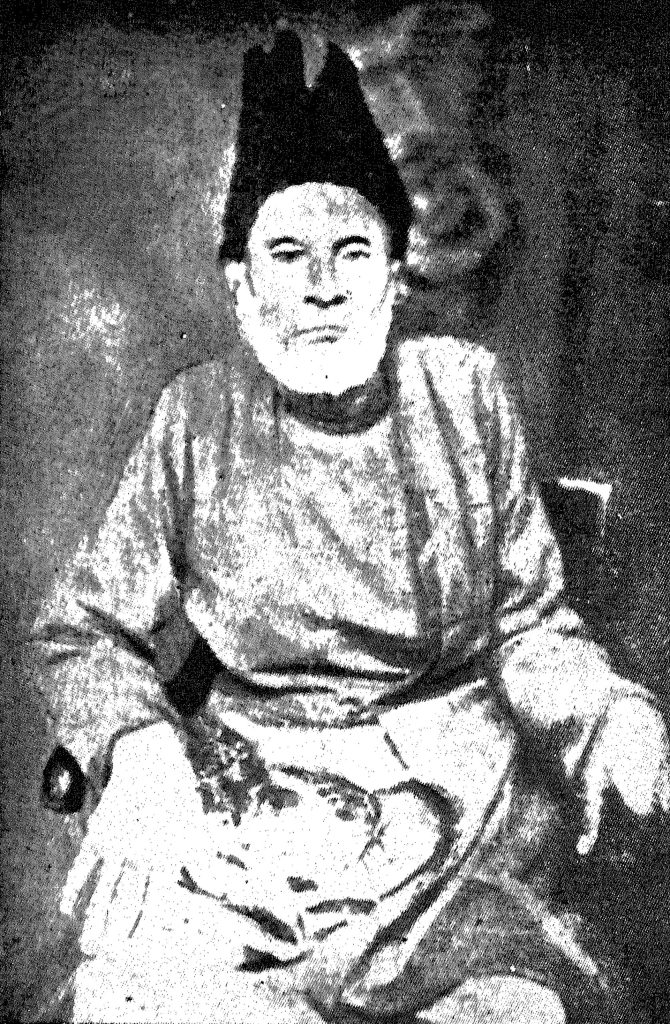An old photograph of Mirza Ghalib seated, in a tall cap