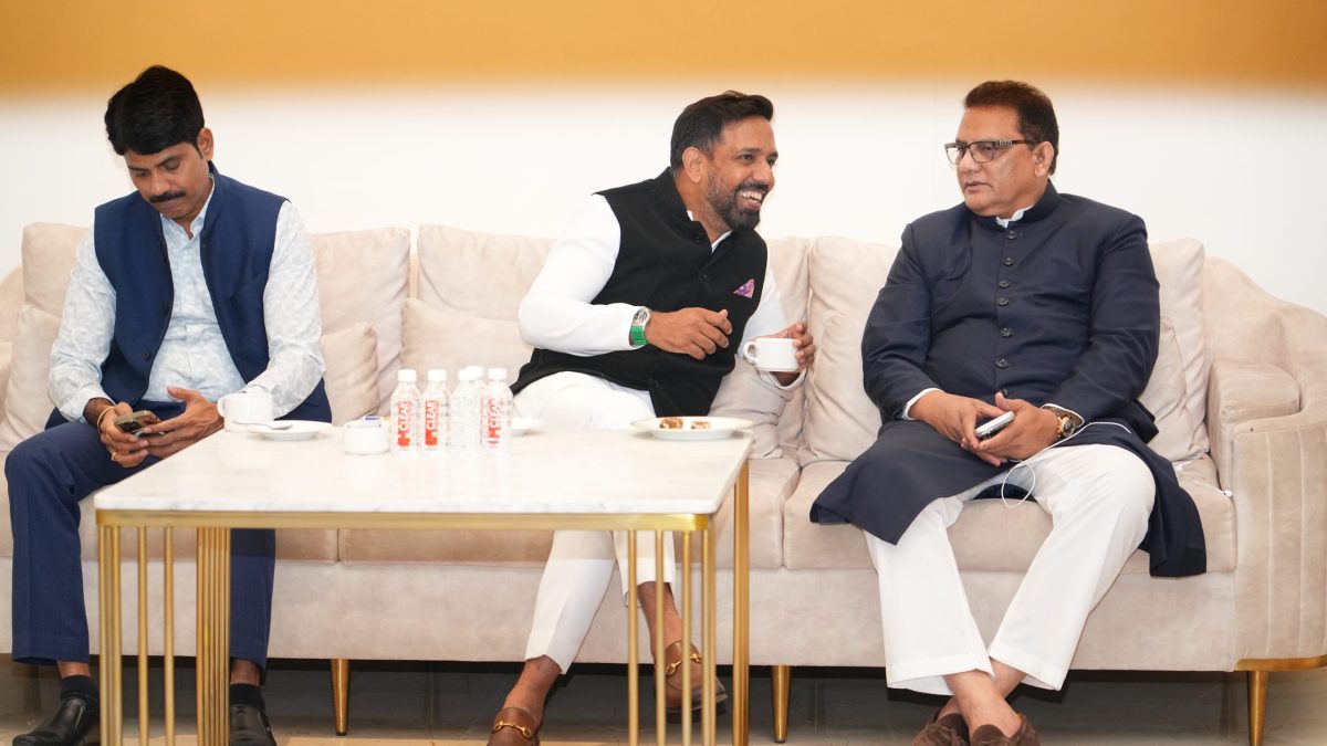 Mohammad Azharuddin in a dark kurta seated on a sofa with two other men
