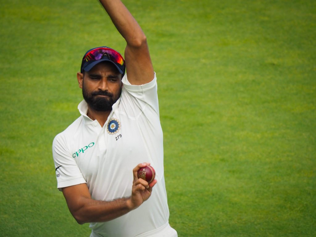 Mohammed Shami in white kit and India cap holding a red cricket ball