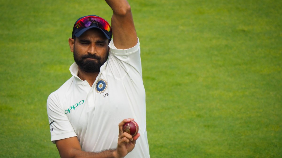 Mohammed Shami in white kit and India cap holding a red cricket ball