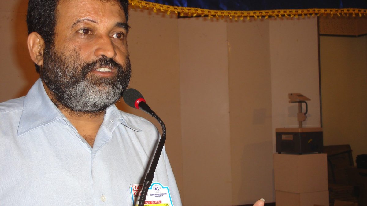 T. V. Mohandas Pai with a beard in a white shirt gesturing as he speaks