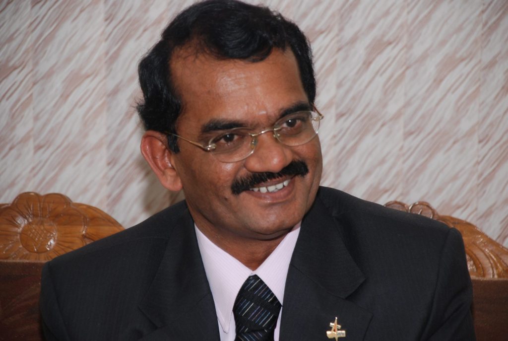 Mylswamy Annadurai in a dark suit, smiling, seated on a sofa