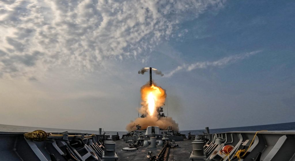 A BrahMos missile lifting off from the deck of an Indian Navy warship in a cloud of flame