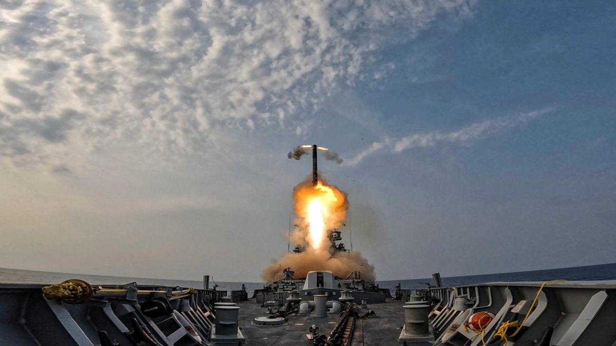 A BrahMos missile lifting off from the deck of an Indian Navy warship in a cloud of flame