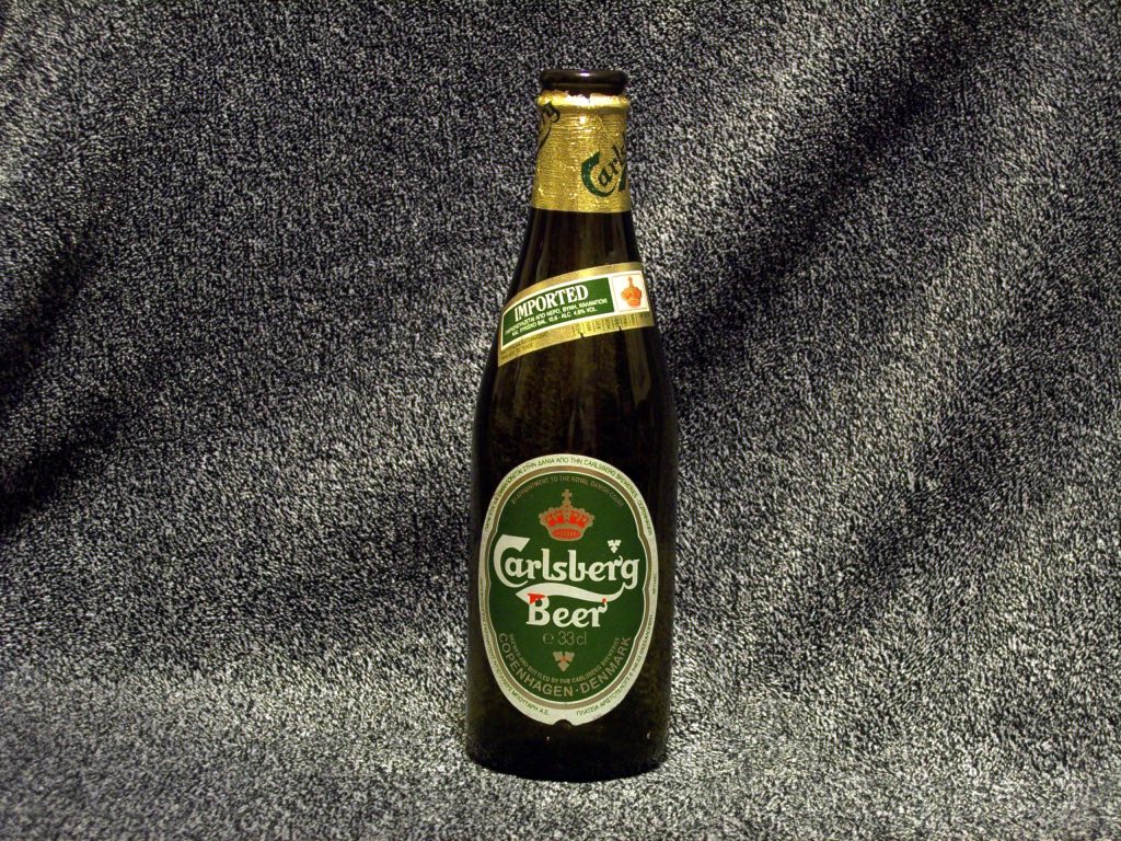 A green bottle of Carlsberg beer standing on a dark surface