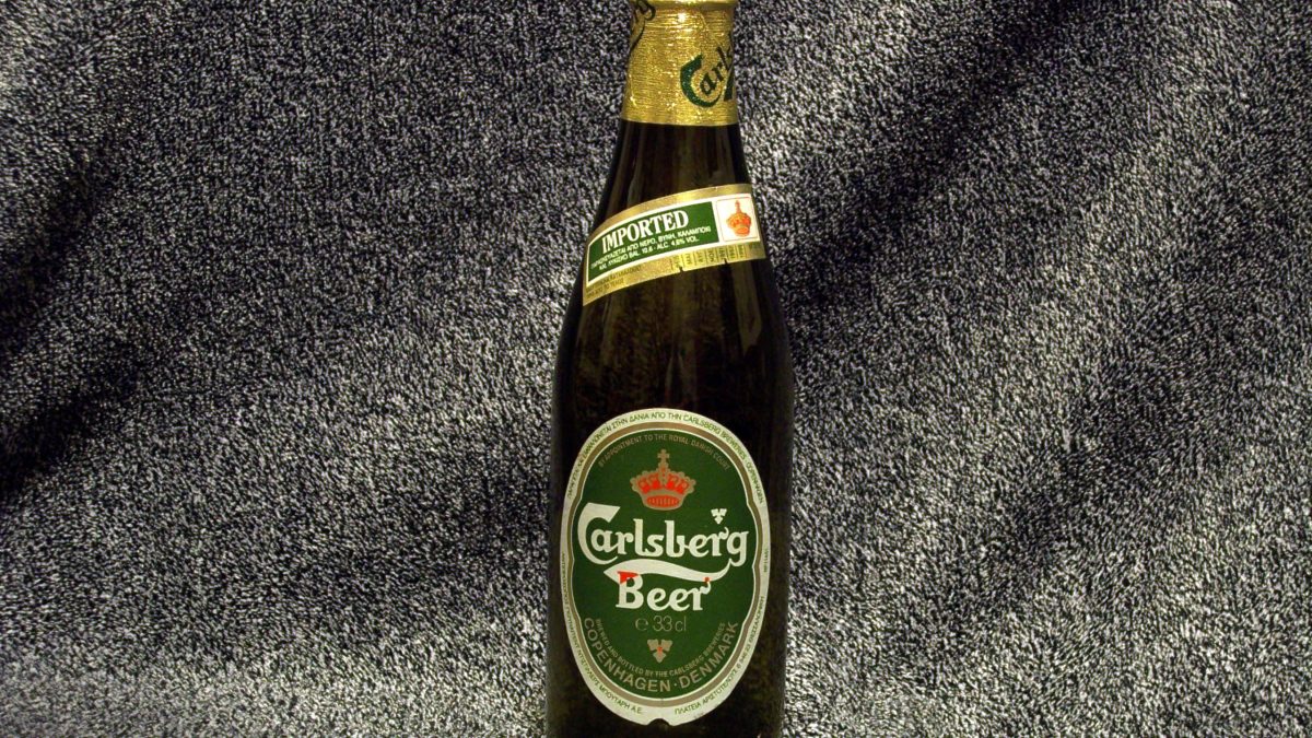 A green bottle of Carlsberg beer standing on a dark surface