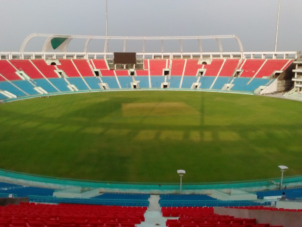 The green outfield and red and blue stands of the Ekana Cricket Stadium in Lucknow