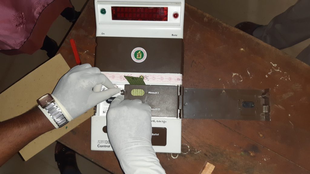 An election official's gloved hand on the control unit of an electronic voting machine