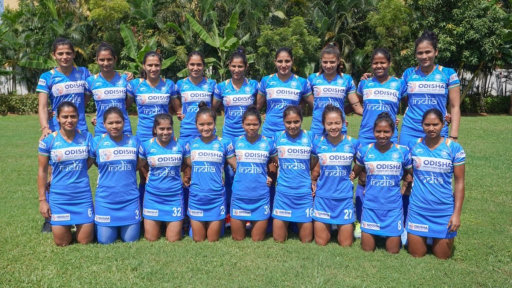 The Indian women's hockey team in blue kit posing in two rows on a pitch