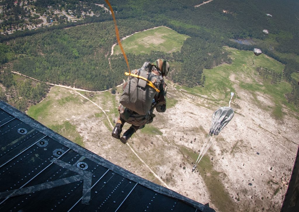 An Indian Army paratrooper stepping off the rear ramp of a helicopter with the ground far below