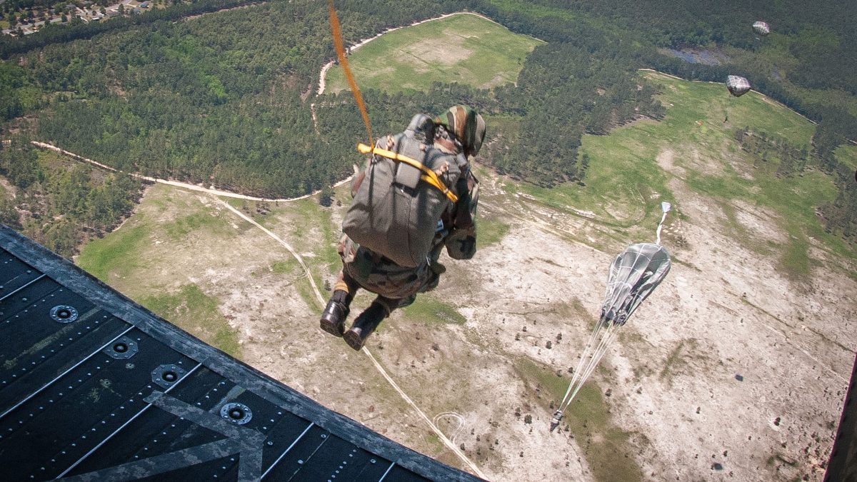 An Indian Army paratrooper stepping off the rear ramp of a helicopter with the ground far below