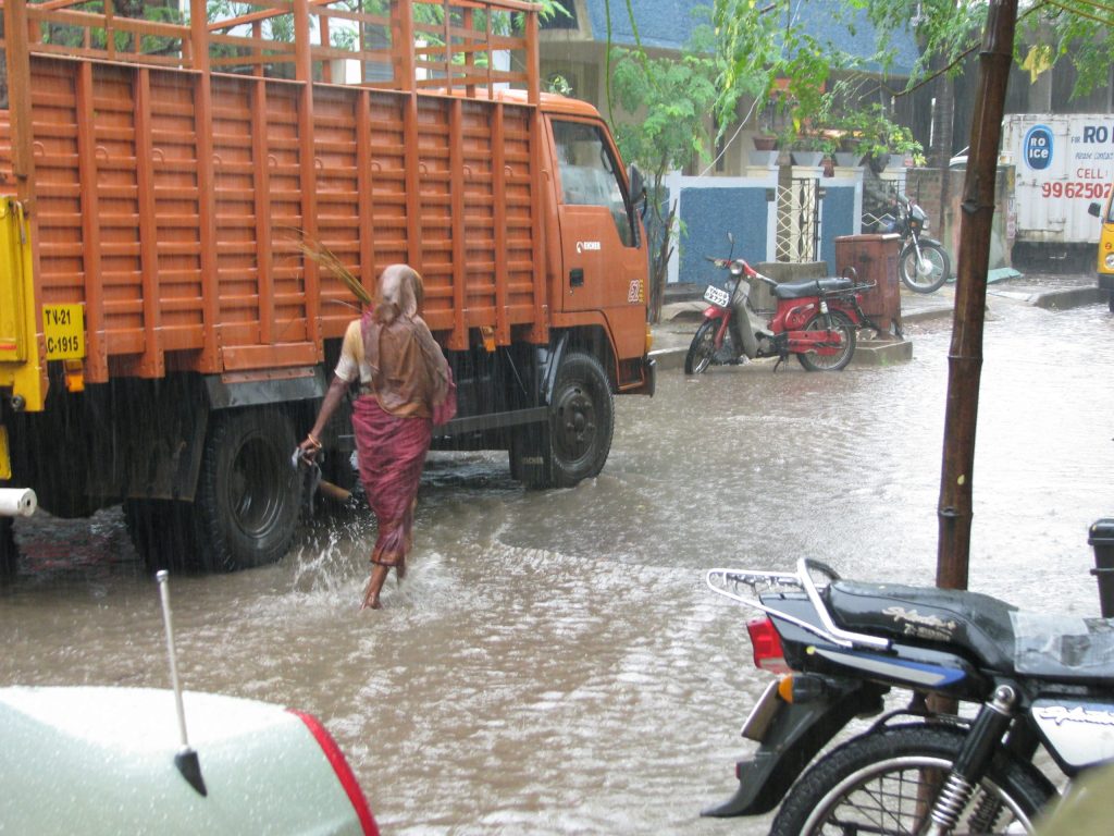 A woman wading across a flooded street past a lorry during monsoon rain in Chennai