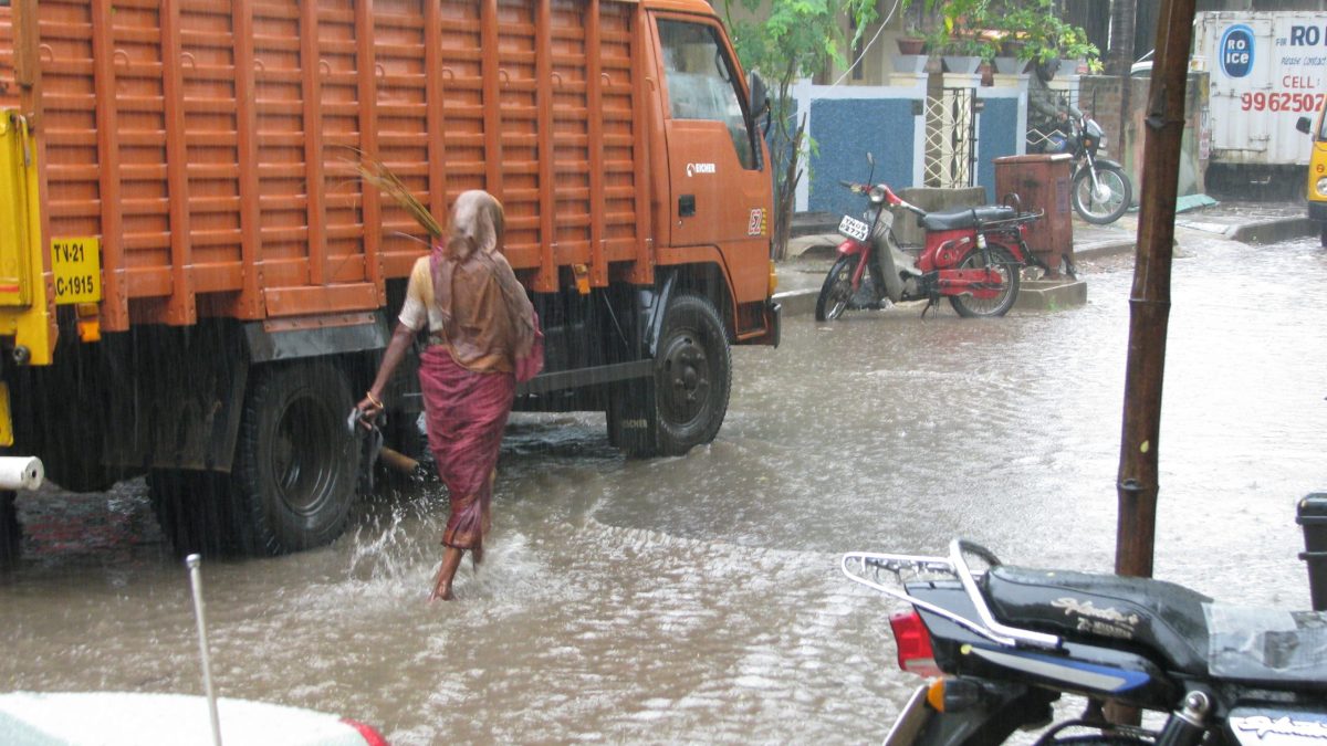 A woman wading across a flooded street past a lorry during monsoon rain in Chennai
