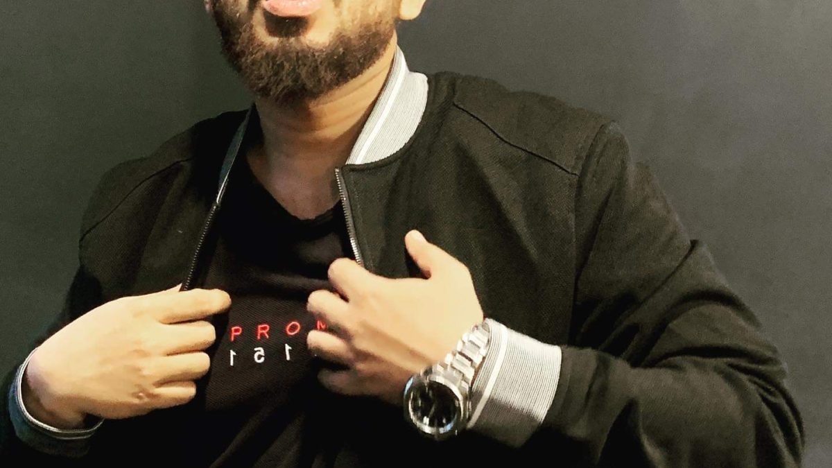 Naezy in a black jacket and tinted glasses, gesturing with both hands