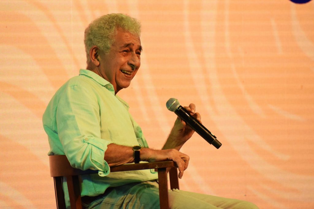 Naseeruddin Shah in a light green kurta, smiling, holding a microphone