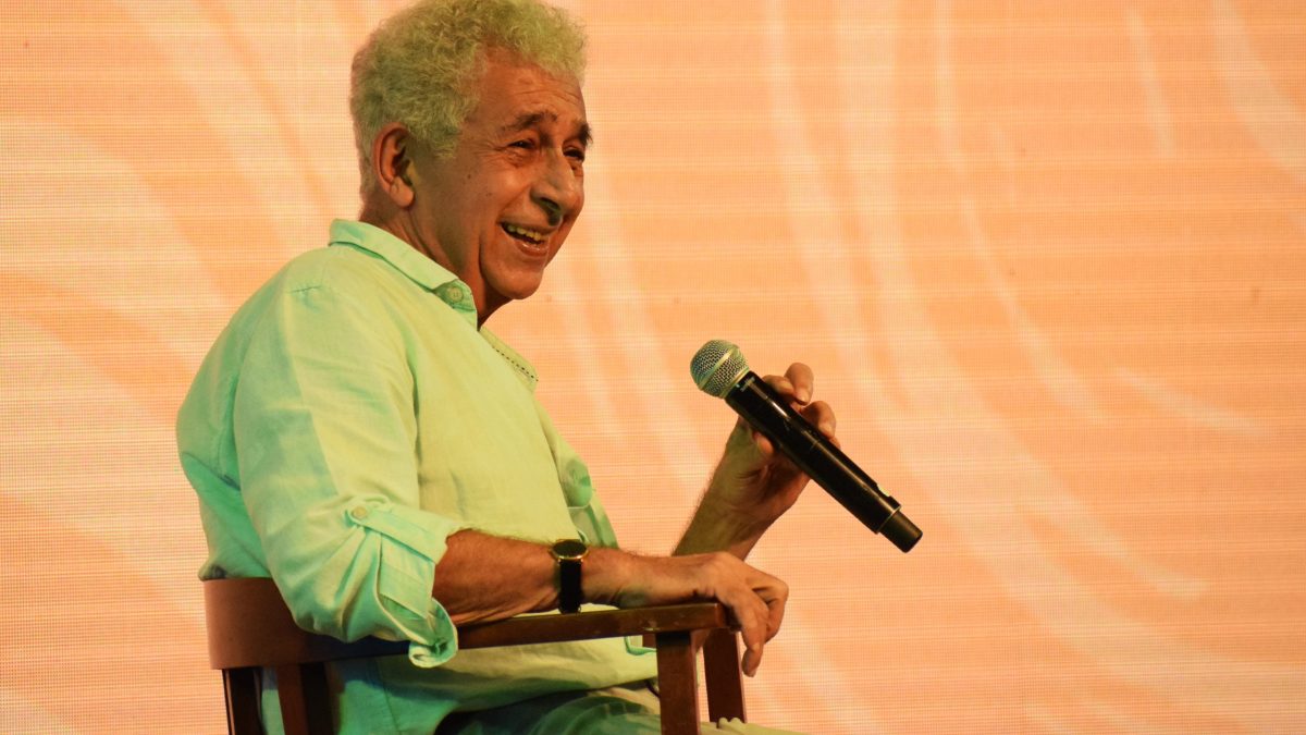 Naseeruddin Shah in a light green kurta, smiling, holding a microphone