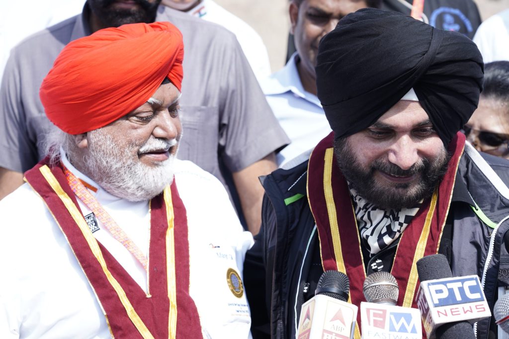 Navjot Singh Sidhu in a black turban laughing beside a man in a red turban