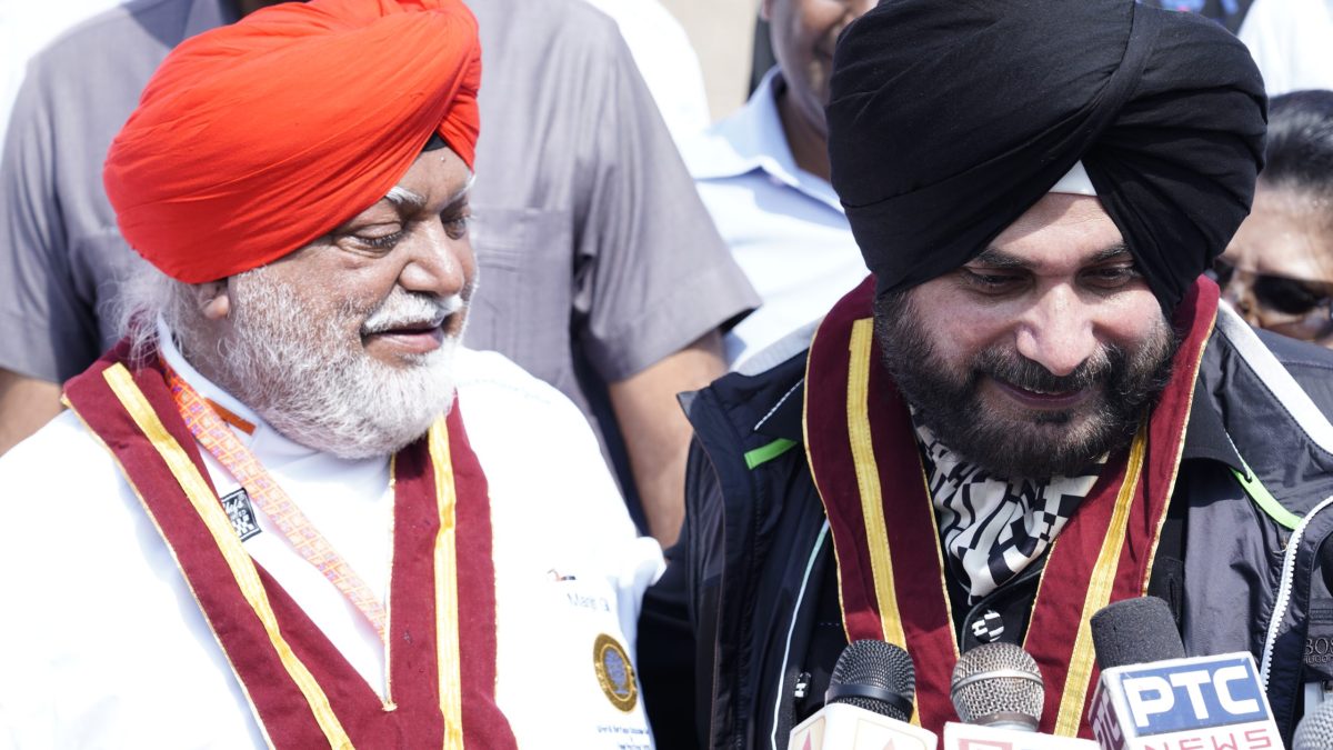 Navjot Singh Sidhu in a black turban laughing beside a man in a red turban