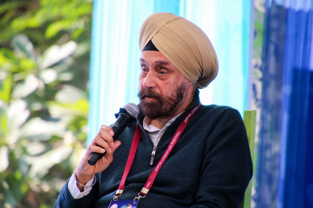 Navtej Sarna in a tan turban and dark jacket speaking into a microphone