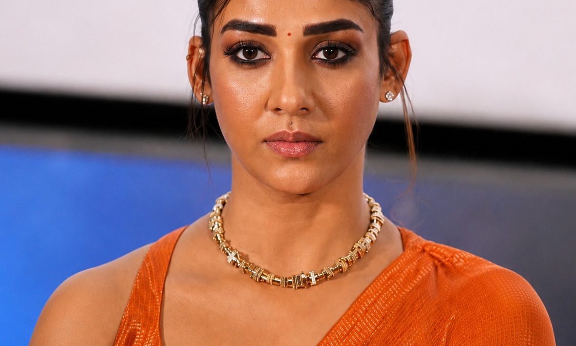 Nayanthara with her hair tied back, in an orange sari and gold necklace