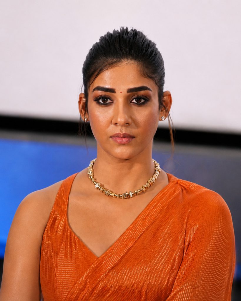 Nayanthara with her hair tied back, in an orange sari and gold necklace