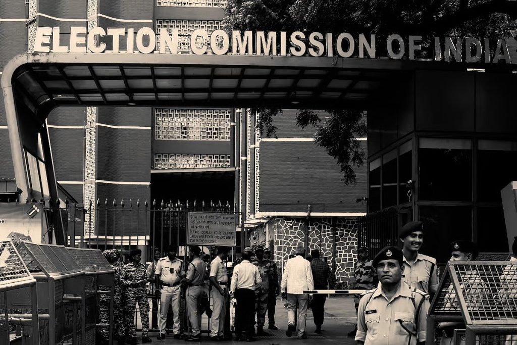 Black-and-white view of the Election Commission of India entrance in New Delhi with security personnel standing in front of it