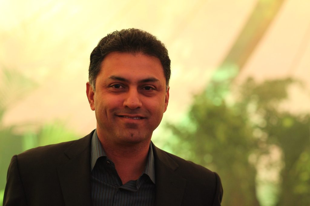 Nikesh Arora in a dark jacket smiling, with greenery behind him