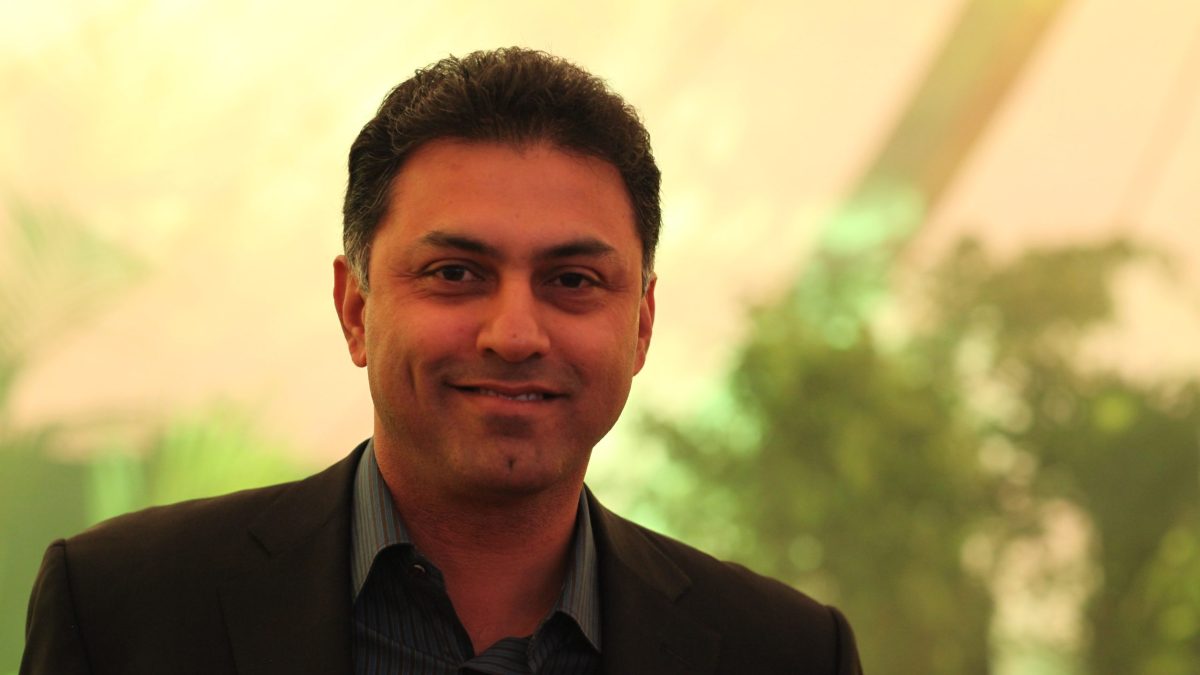Nikesh Arora in a dark jacket smiling, with greenery behind him