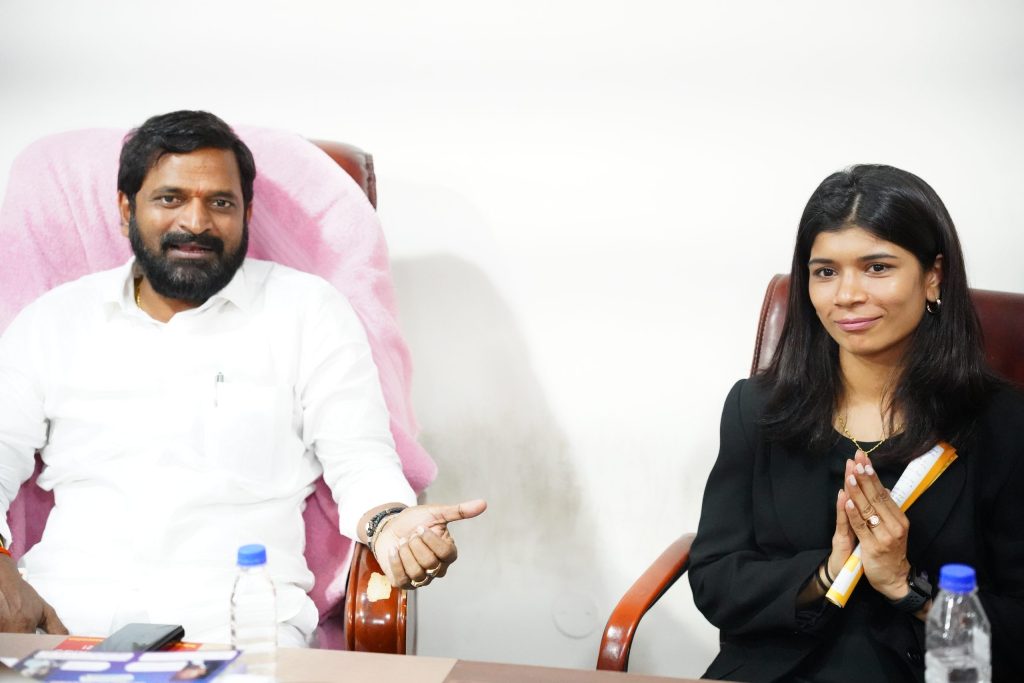 Nikhat Zareen in a black jacket with folded hands, seated beside Telangana's sports minister