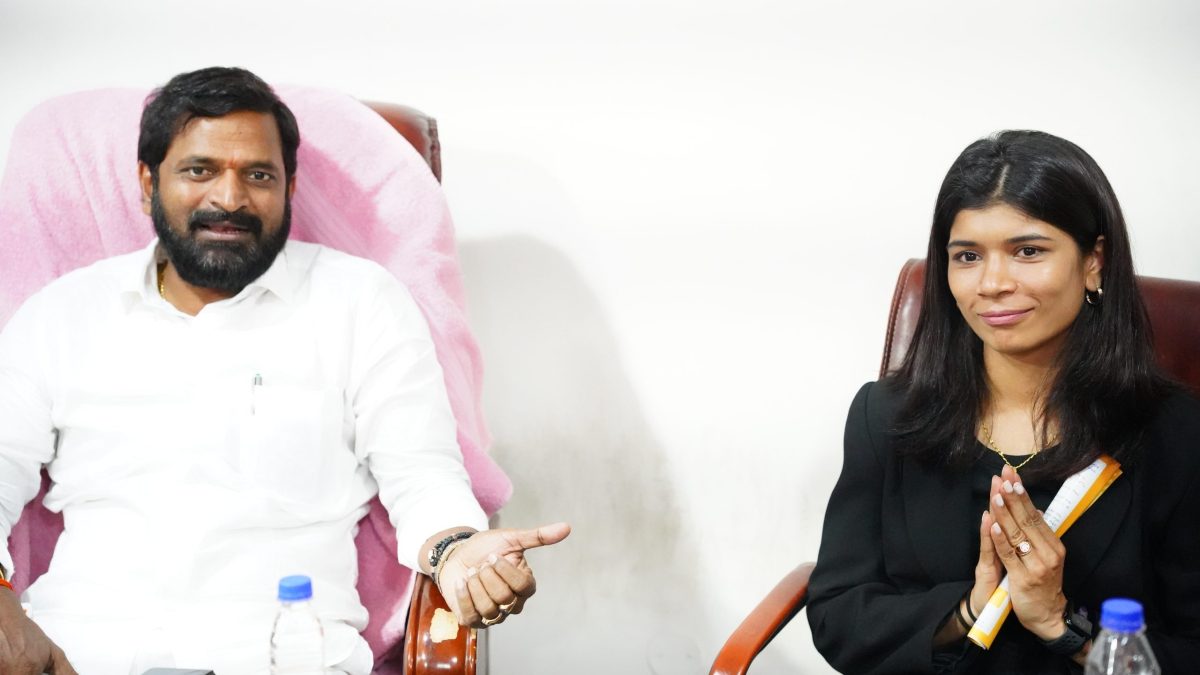 Nikhat Zareen in a black jacket with folded hands, seated beside Telangana's sports minister