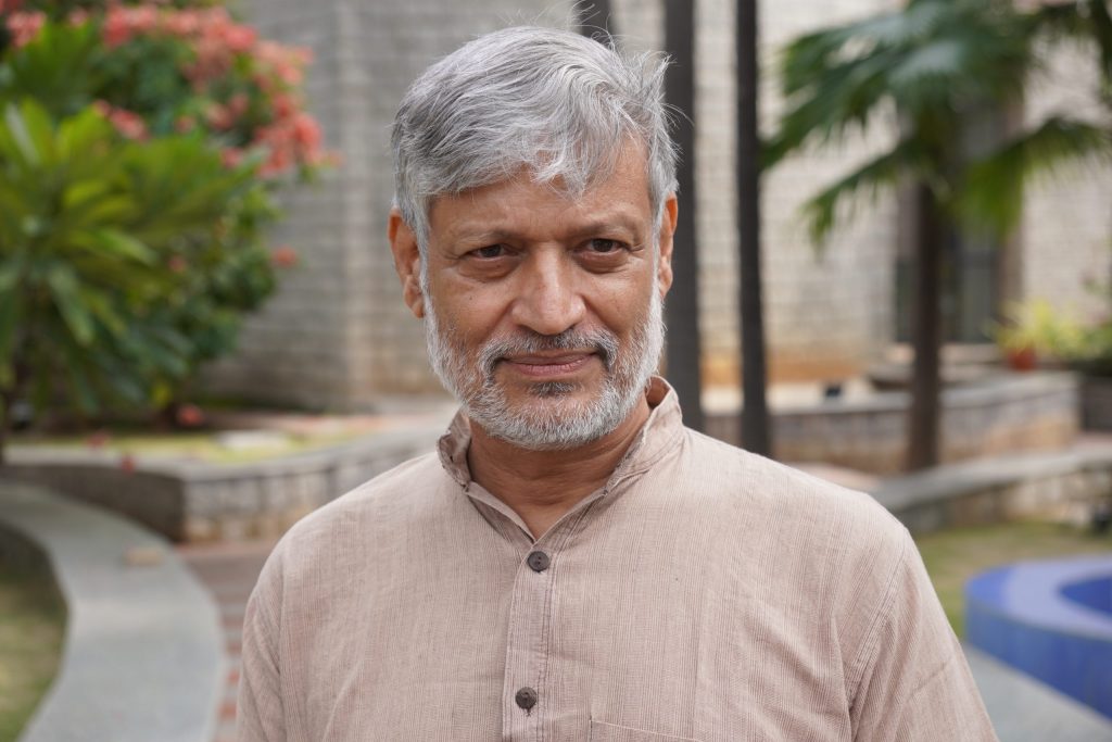 Nikhil Dey with grey hair and beard in a khadi kurta standing in a garden