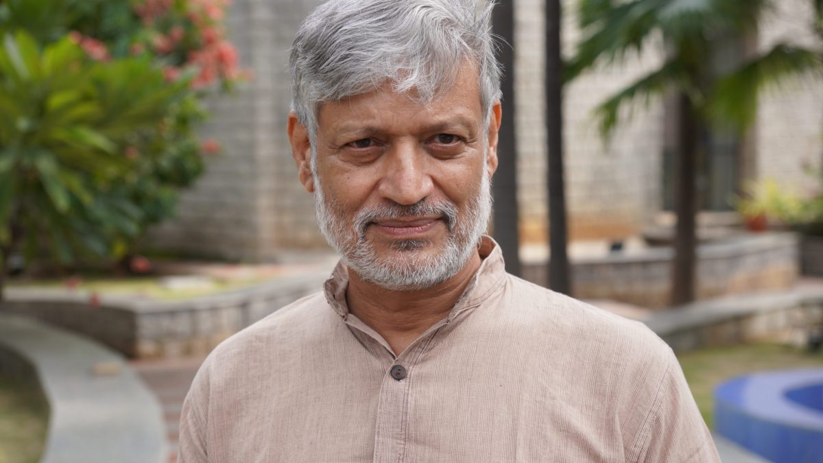 Nikhil Dey with grey hair and beard in a khadi kurta standing in a garden