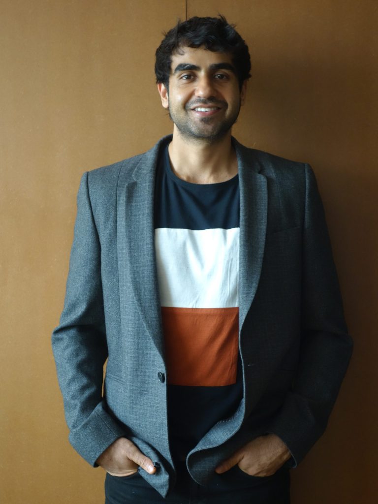 Nikhil Kamath smiling in a grey blazer and striped T-shirt