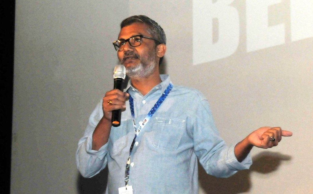 Nitesh Tiwari in glasses and a light blue shirt speaking into a microphone and gesturing
