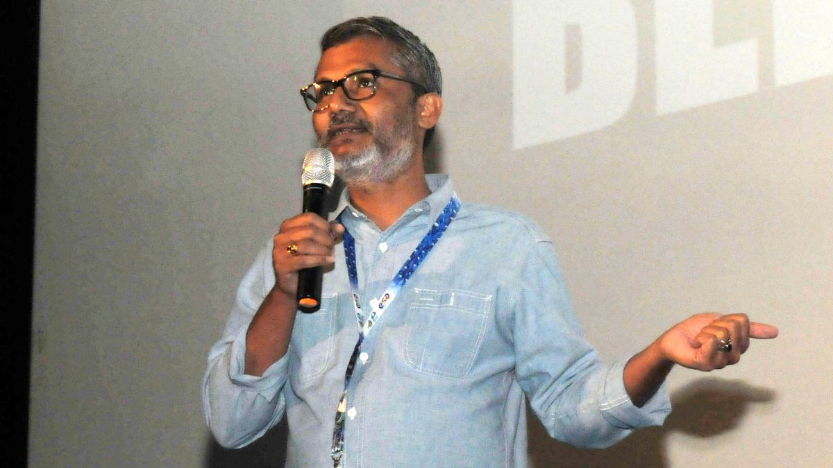 Nitesh Tiwari in glasses and a light blue shirt speaking into a microphone and gesturing