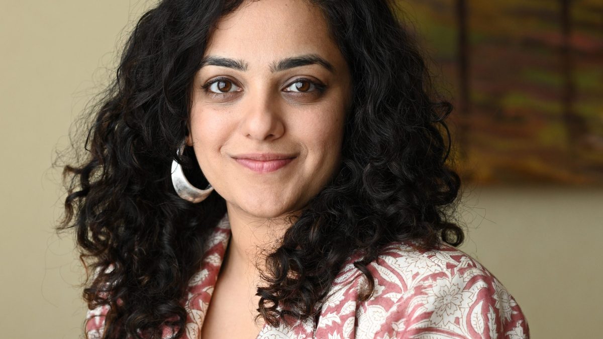 Nithya Menen with curly hair and a silver earring smiling at the camera