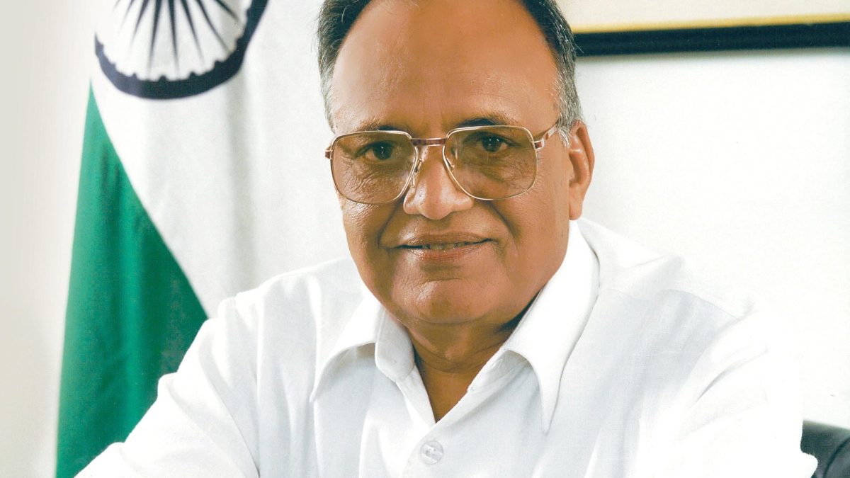 O. P. Jindal in a white shirt, arms folded, beside the national flag