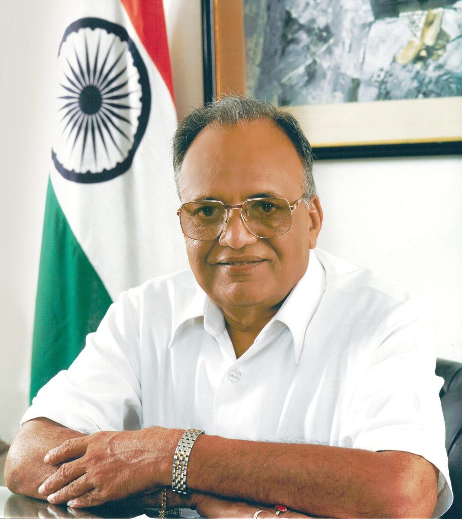 O. P. Jindal in a white shirt, arms folded, beside the national flag