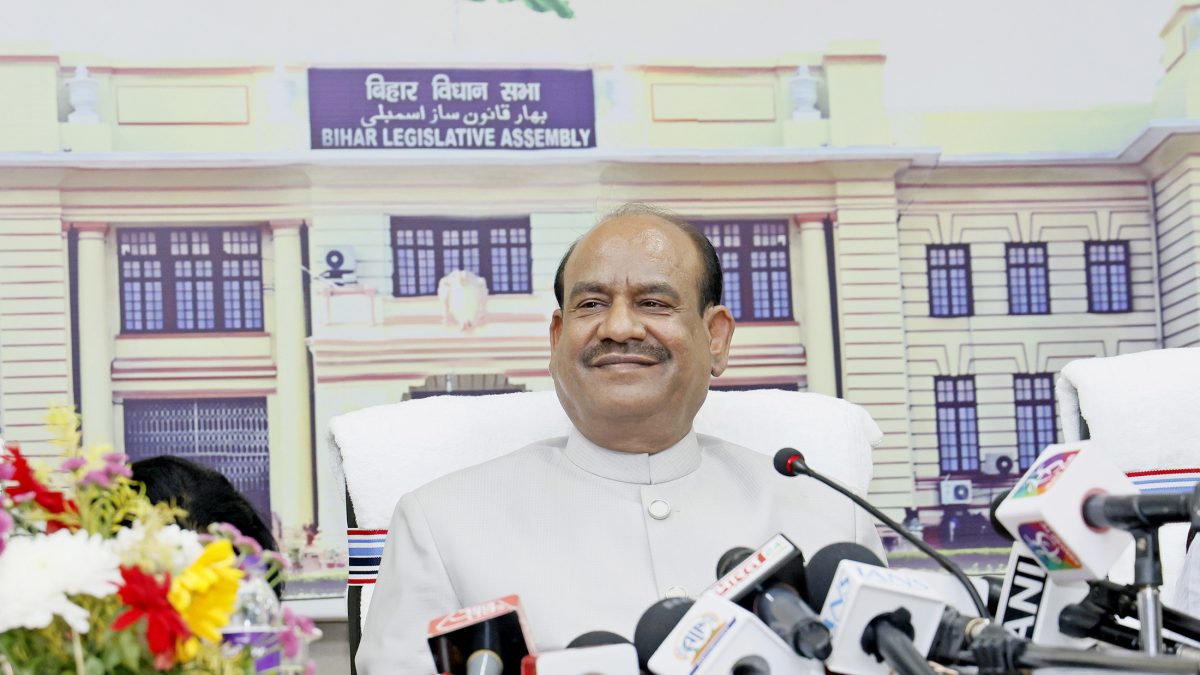 Om Birla in a white kurta and waistcoat smiling as he speaks to the press