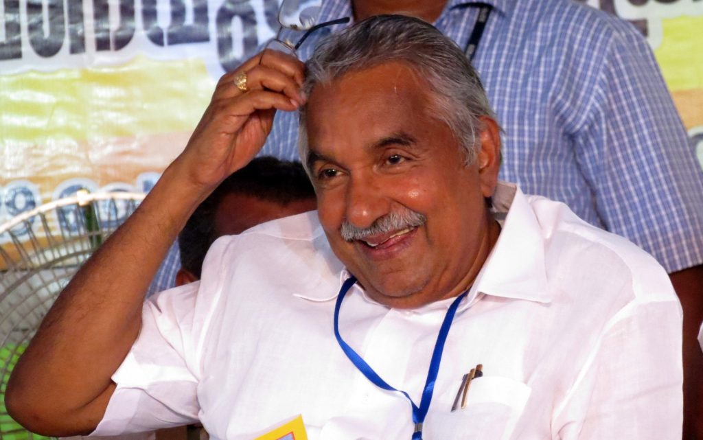 Oommen Chandy with tousled grey hair in a white shirt, smiling and touching his head