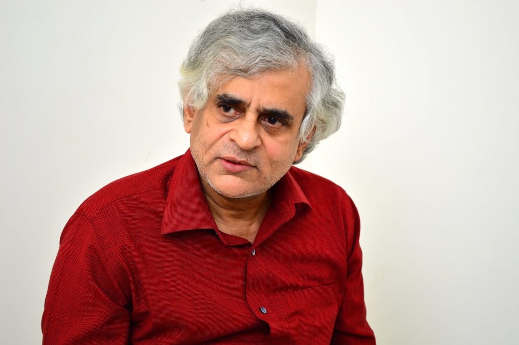 Portrait of P. Sainath with grey hair, wearing a red shirt