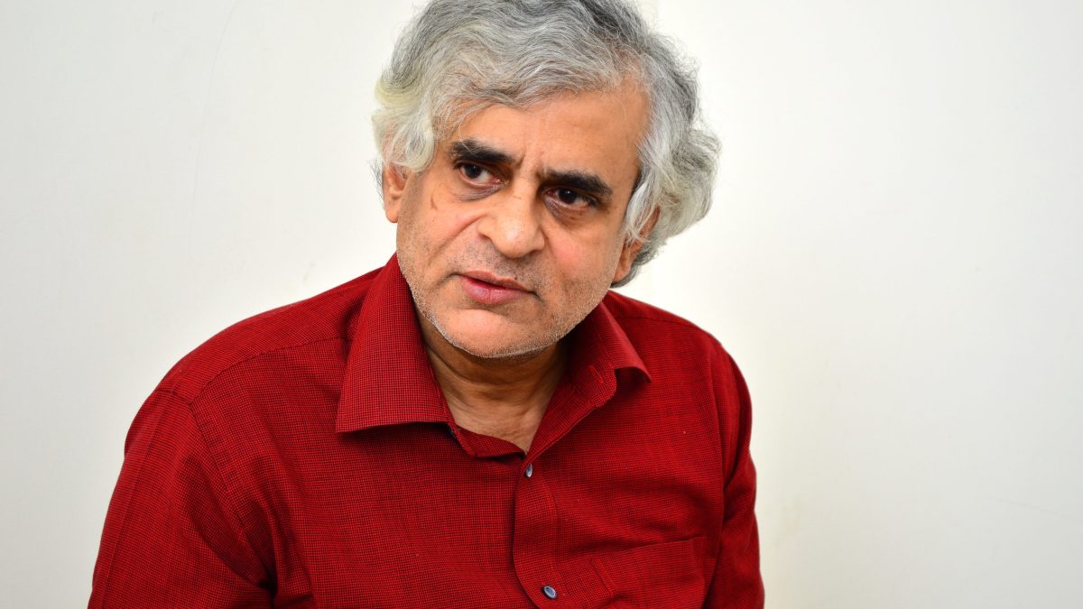 Portrait of P. Sainath with grey hair, wearing a red shirt